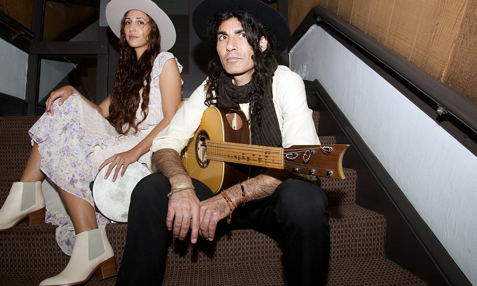 Nahti with a tambourine and Erez with a guitar, seated together on a carpeted stairway