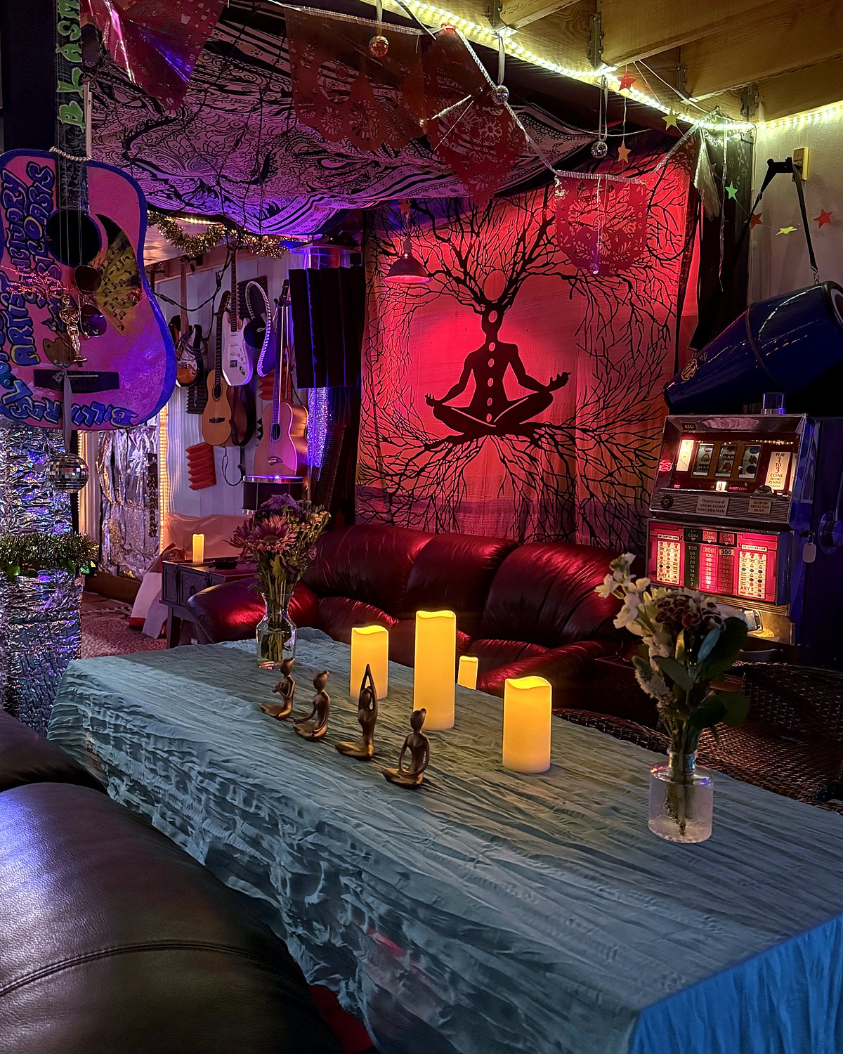 Candles and small brass figures on a pale blue cloth in front of a red lit tree of life tapestry