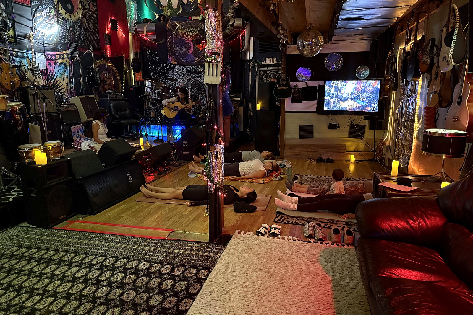 Guests lying on yoga mats in deep relaxation while Nahti and Erez play from the stage of a candle lit music room
